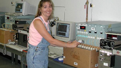 A woman indoors with several electronic equipment beside her