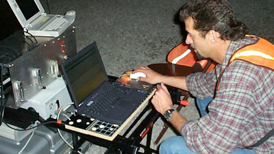 Man seated in front of a makeshift table holding a computer mouse with a couple of laptop in front